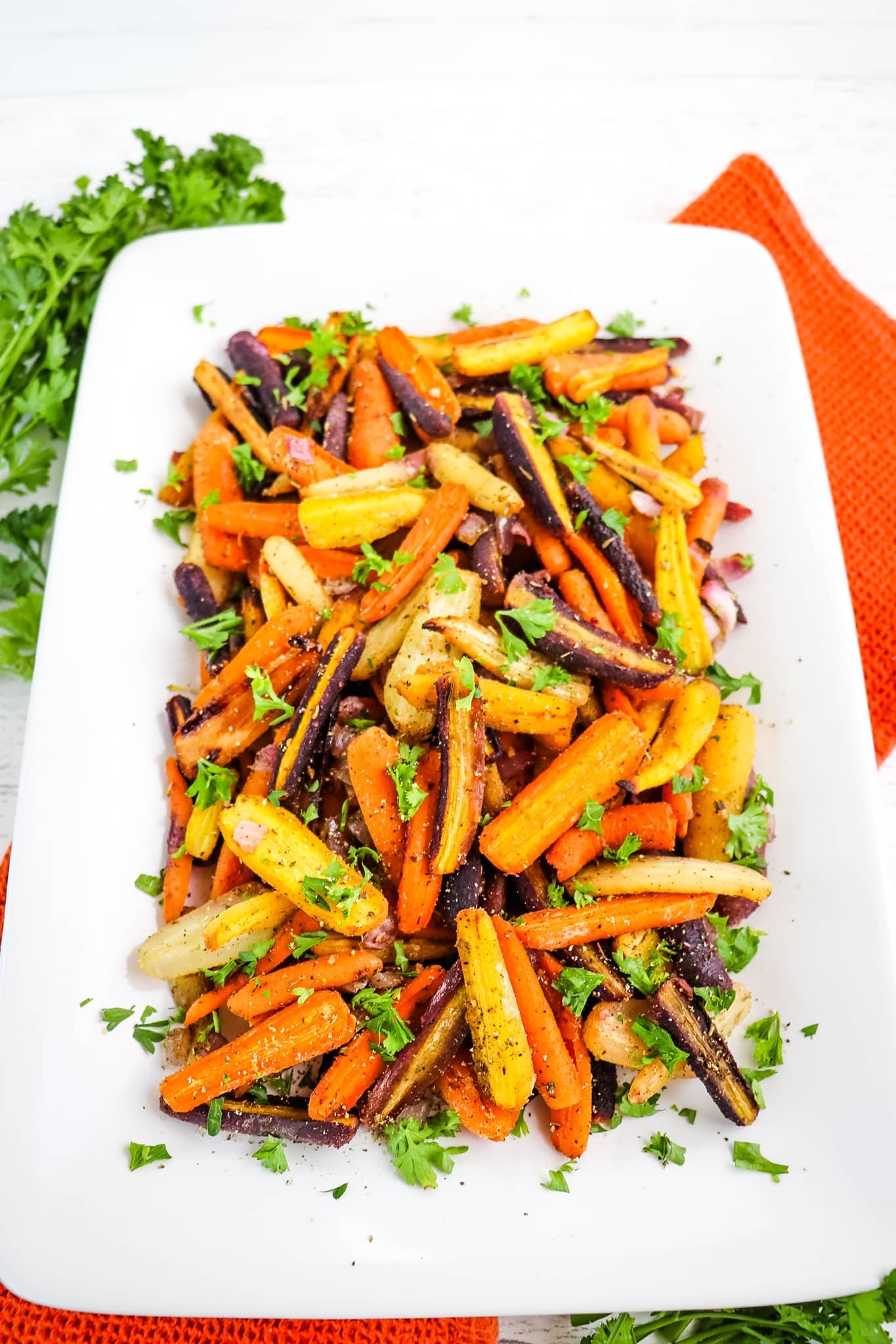 Roasted rainbow carrots topped with parsley on white platter.