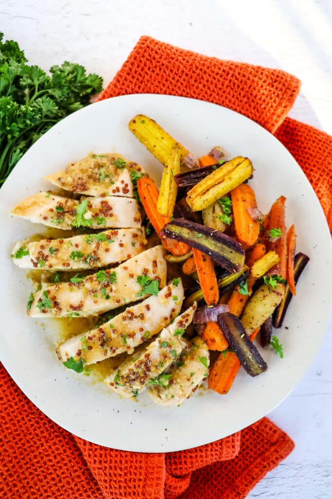 Roasted rainbow carrots on plate with sliced chicken breast.