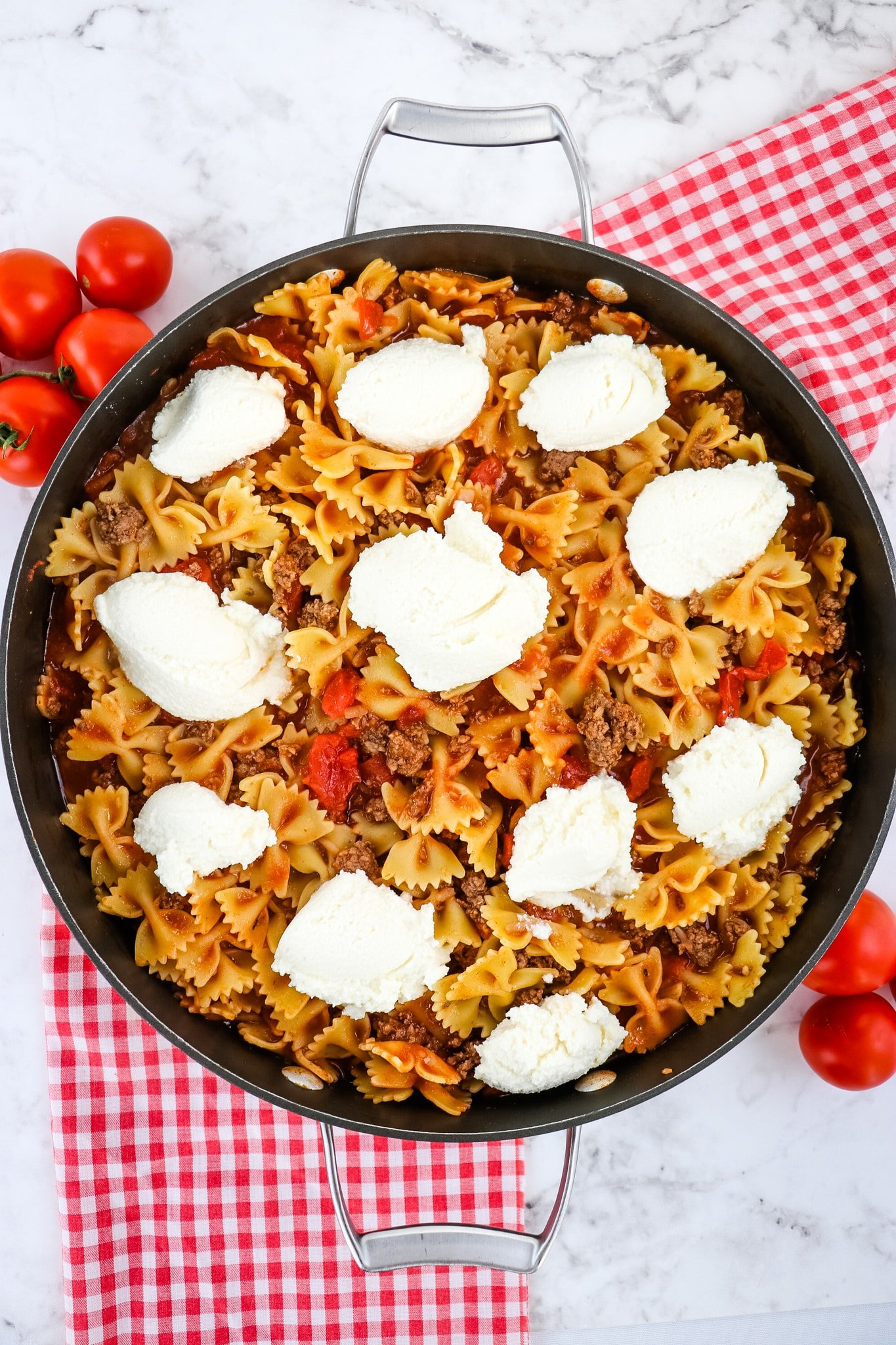 Dollops of ricotta cheese being added to skillet lasagna.