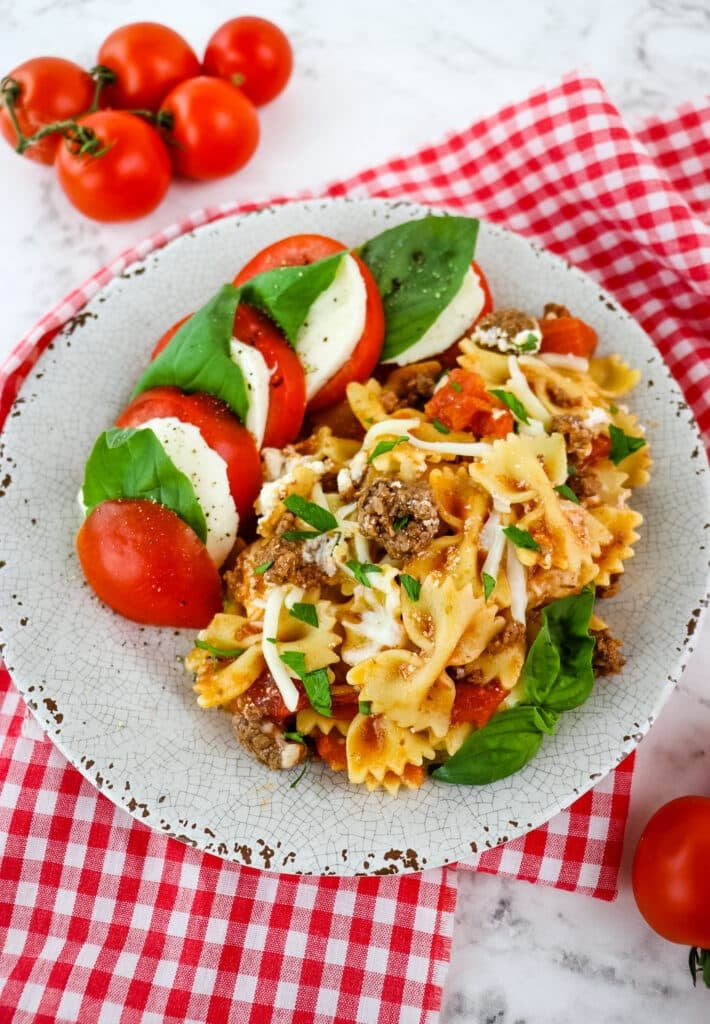 Skillet lasagna on plate with caprese salad and fresh basil leaves.