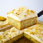 Moist banana cake with cream cheese frosting being lifted out of pan.
