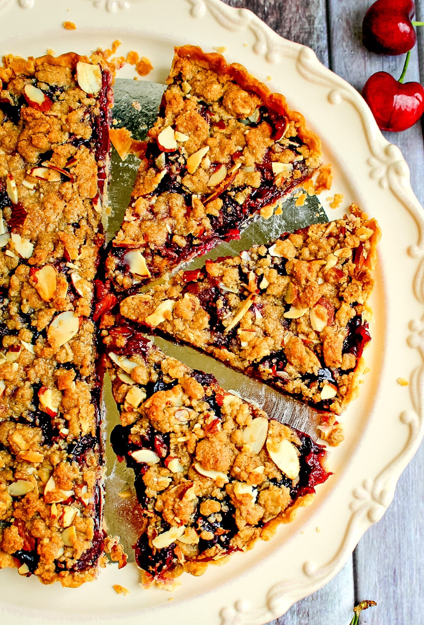 Sliced cherry tart on platter with fresh cherries on the side.