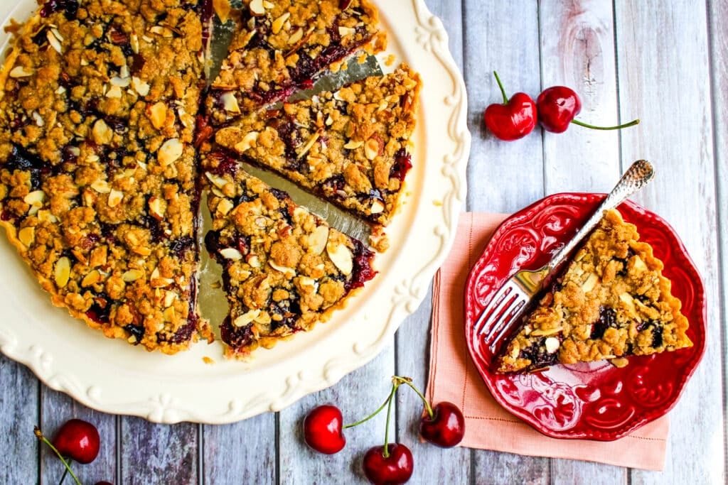 Cherry tart recipe on platter with single slice on plate.