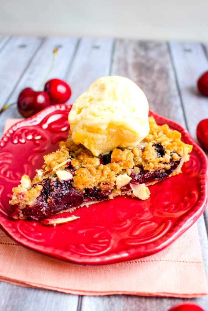 Cherry tart slice on plate topped with a scoop of vanilla ice cream.