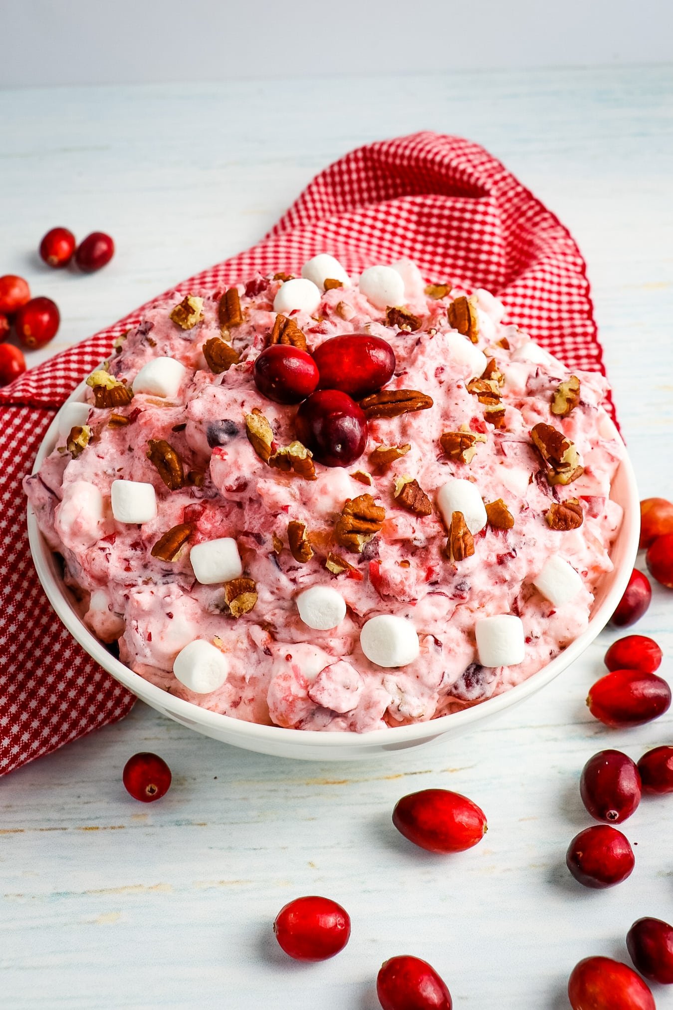 Cranberry fluff salad in a bowl topped with fresh cranberries, chopped pecans and marshmallows.