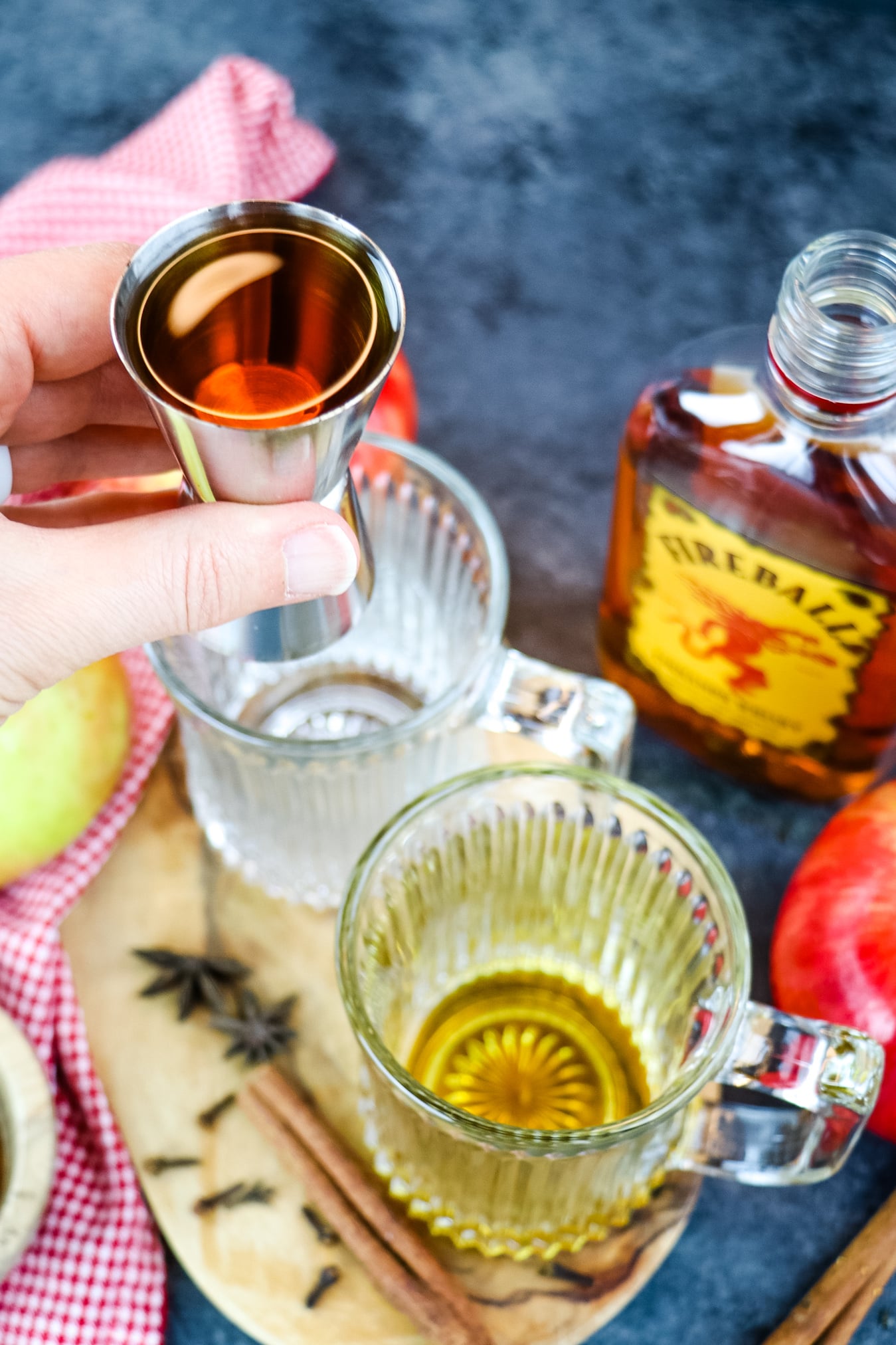 Fireball whiskey being added to mugs for apple cider hot toddy.