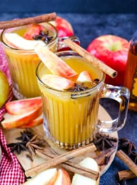 Two mugs of Fireball apple cider hot toddy, topped with apple slices and cinnamon sticks.