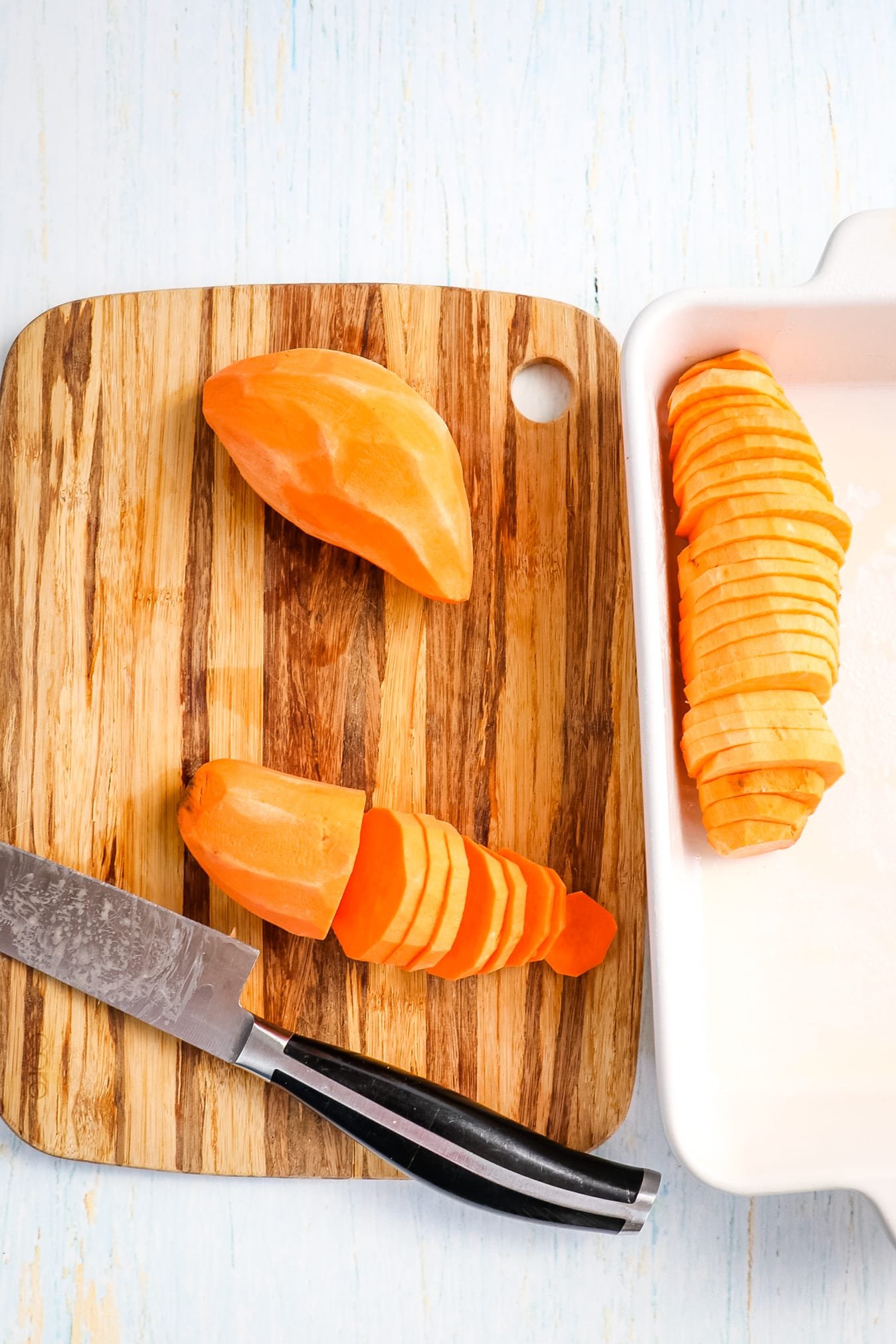 Hasselback sweet potatoes being sliced and placed in baking dish.