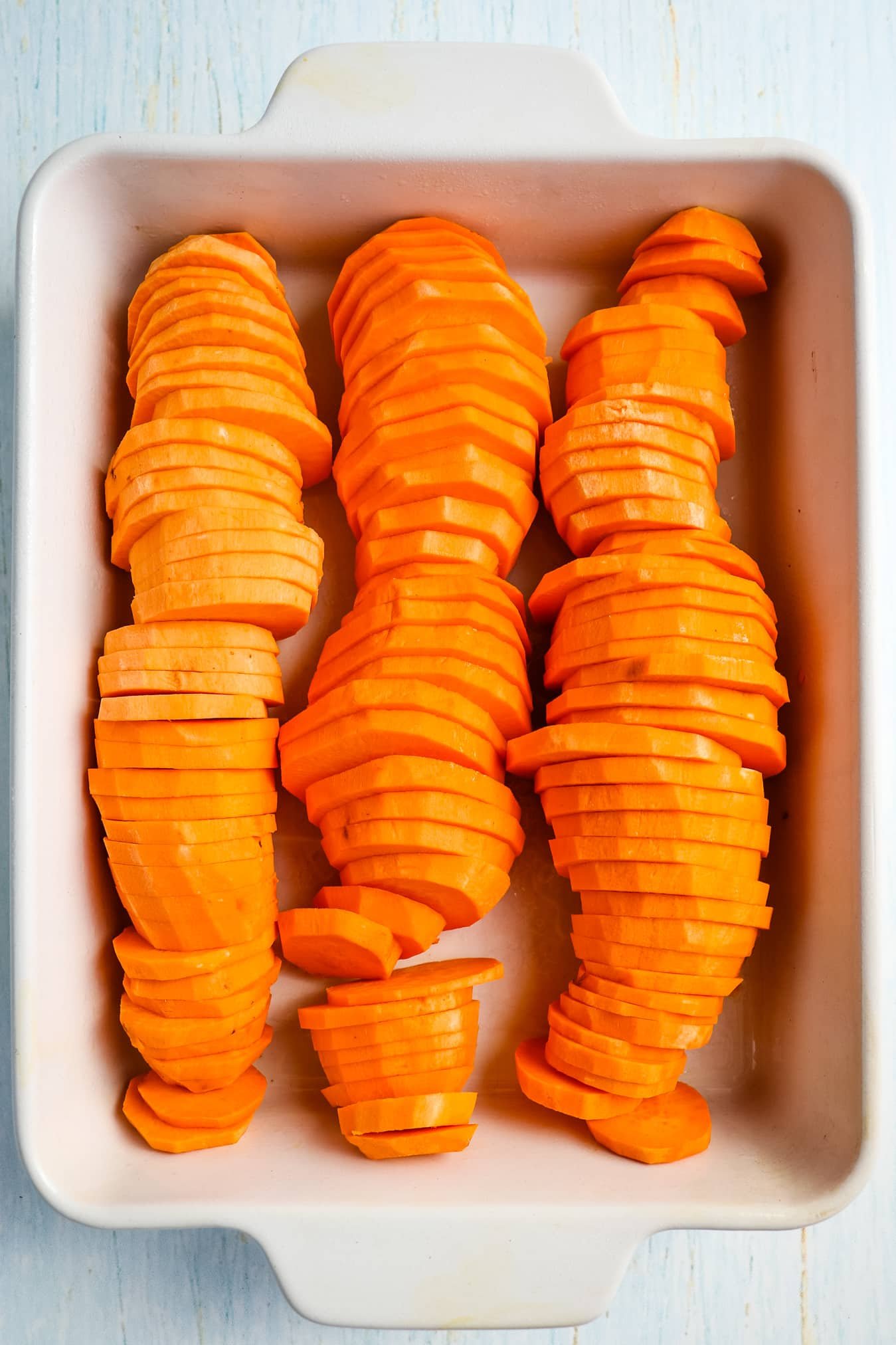 Sliced sweet potatoes filling a baking dish.