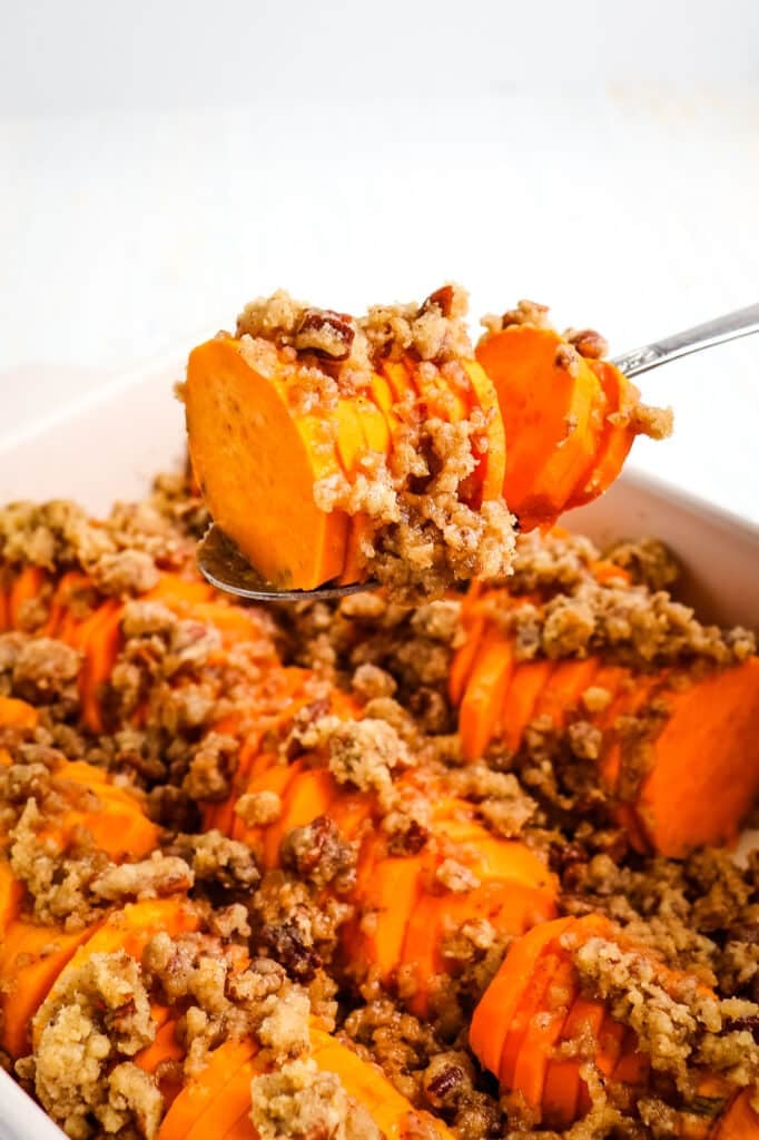 Hasselback sweet potatoes being spooned out of casserole dish.