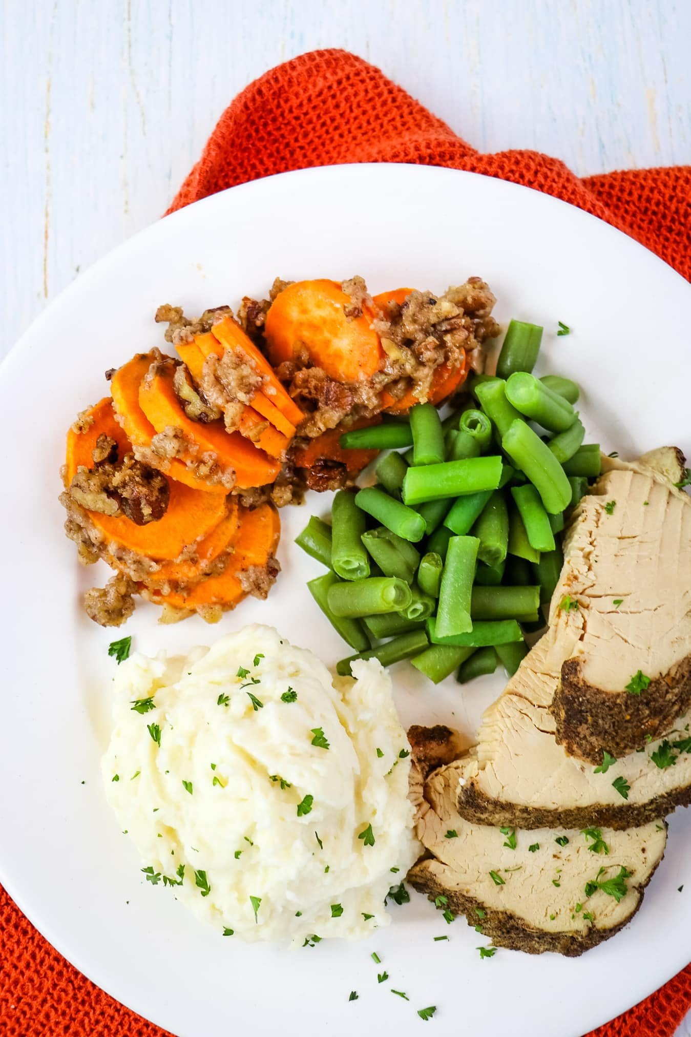 Hasselback sweet potatoes on plate with turkey, mashed potatoes and green beans.