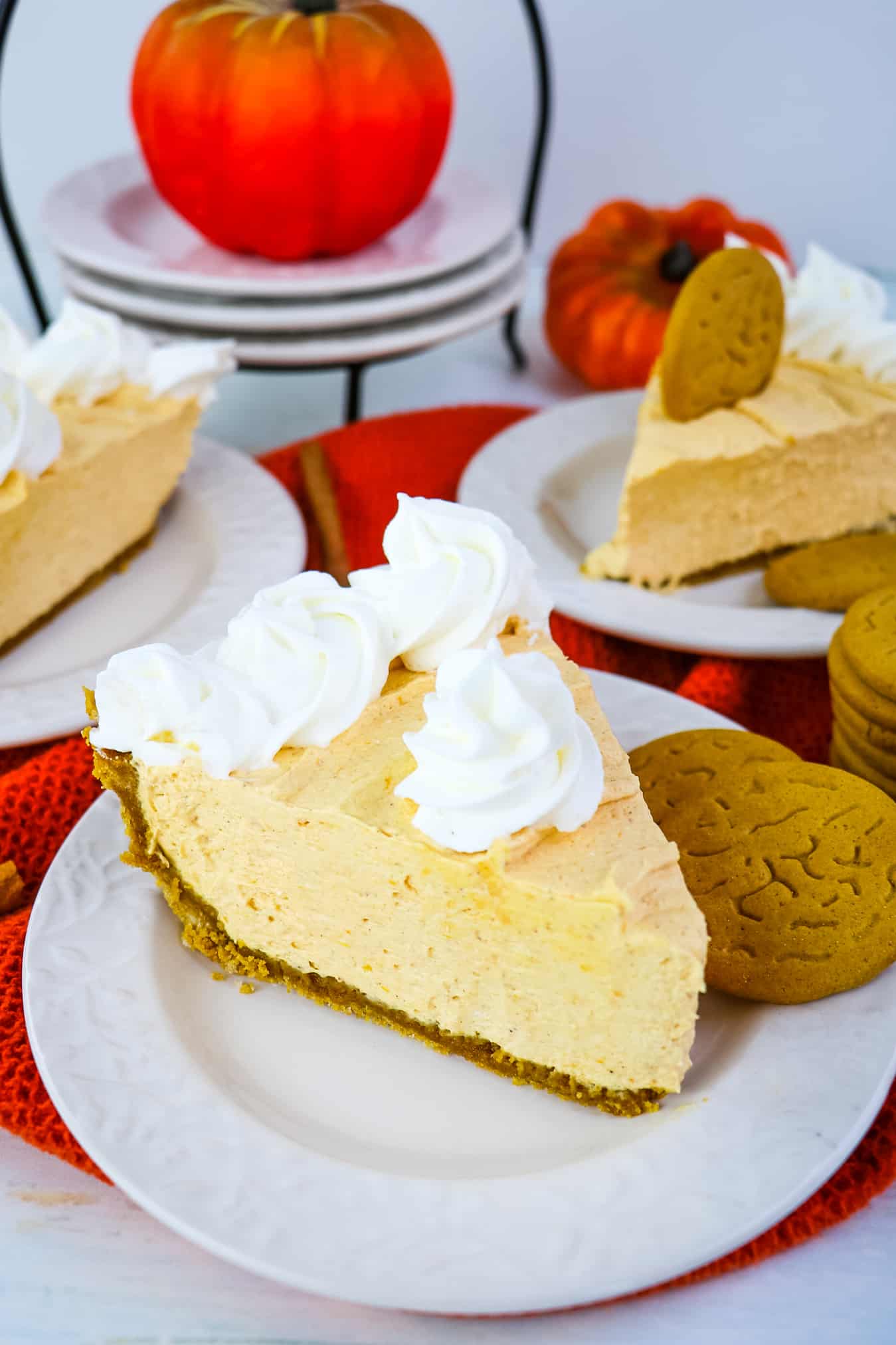 Three slices of no bake pumpkin pie on white plates, with pumpkins in the background.