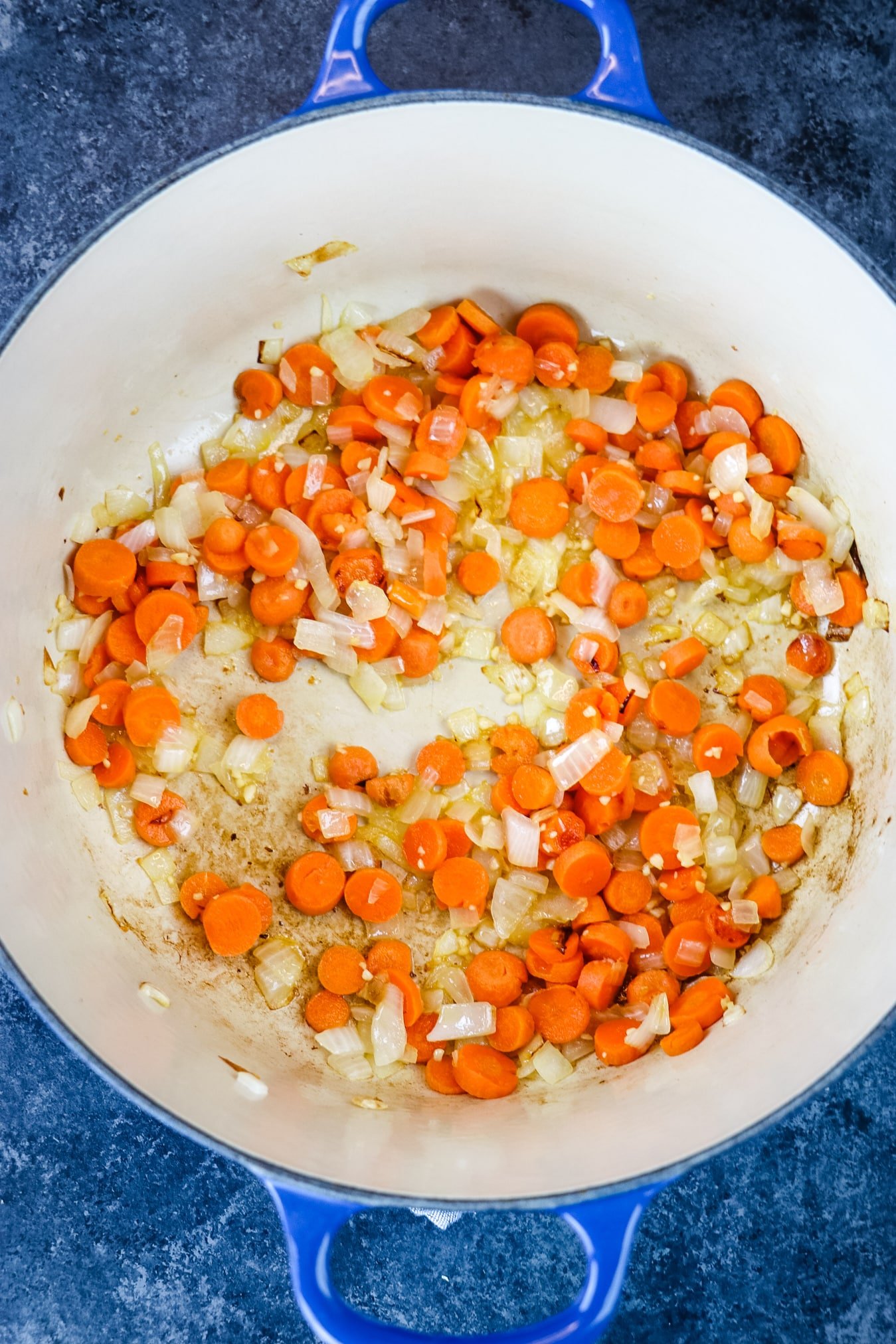 Carrots, onions and garlic at the bottom of a Dutch oven being sauteed.