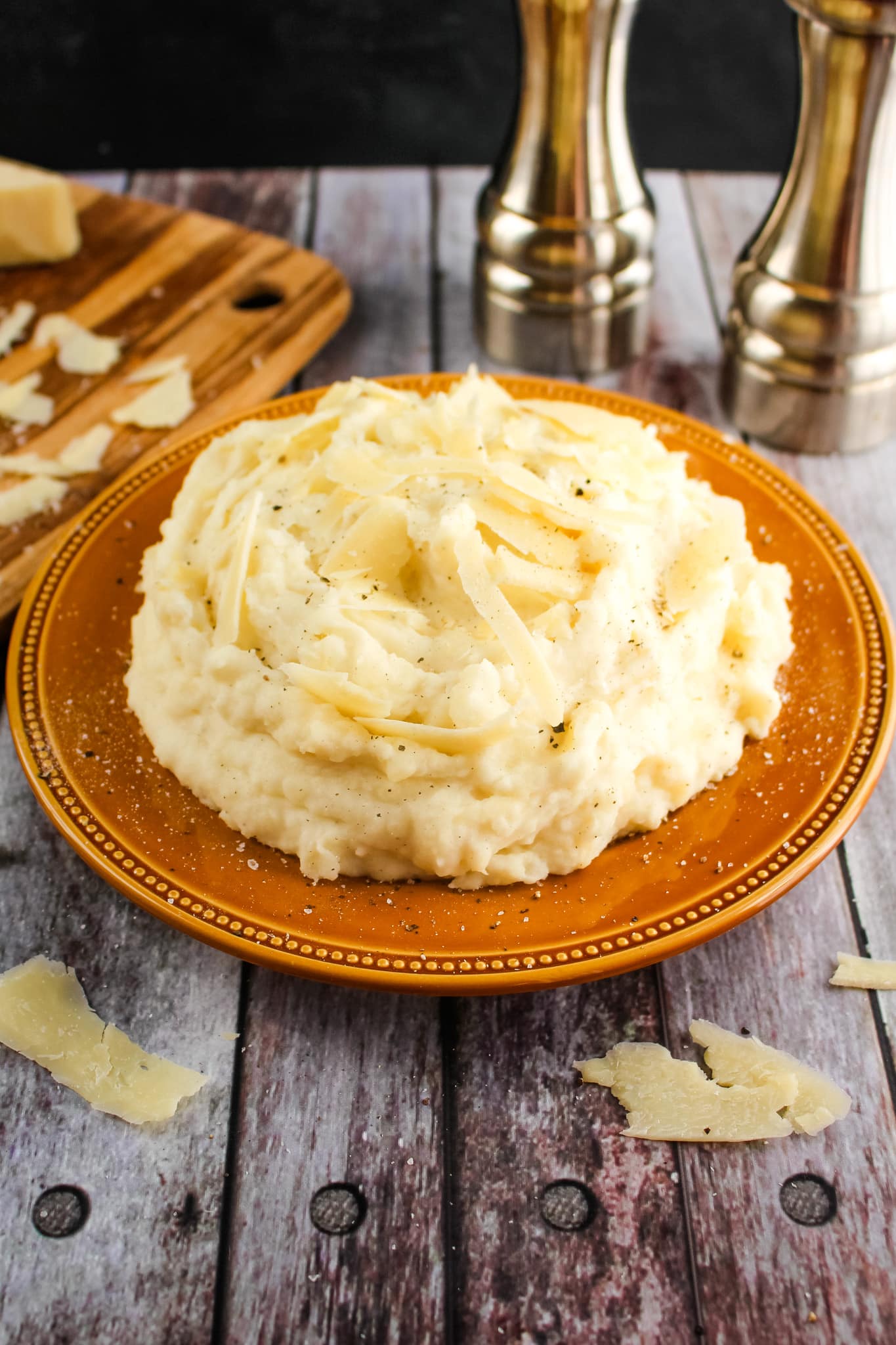 Parmesan mashed potatoes on a platter topped with shaved Parmesan cheese.