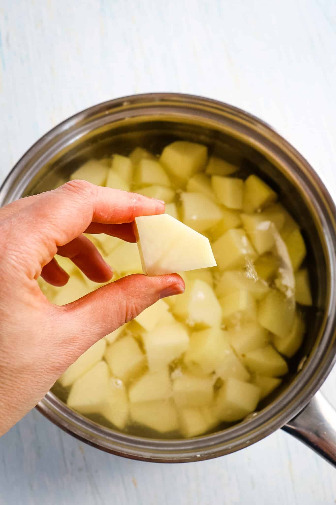 Piece of potato held in hand to show how big to cut potatoes for making parmesan mashed potatoes.
