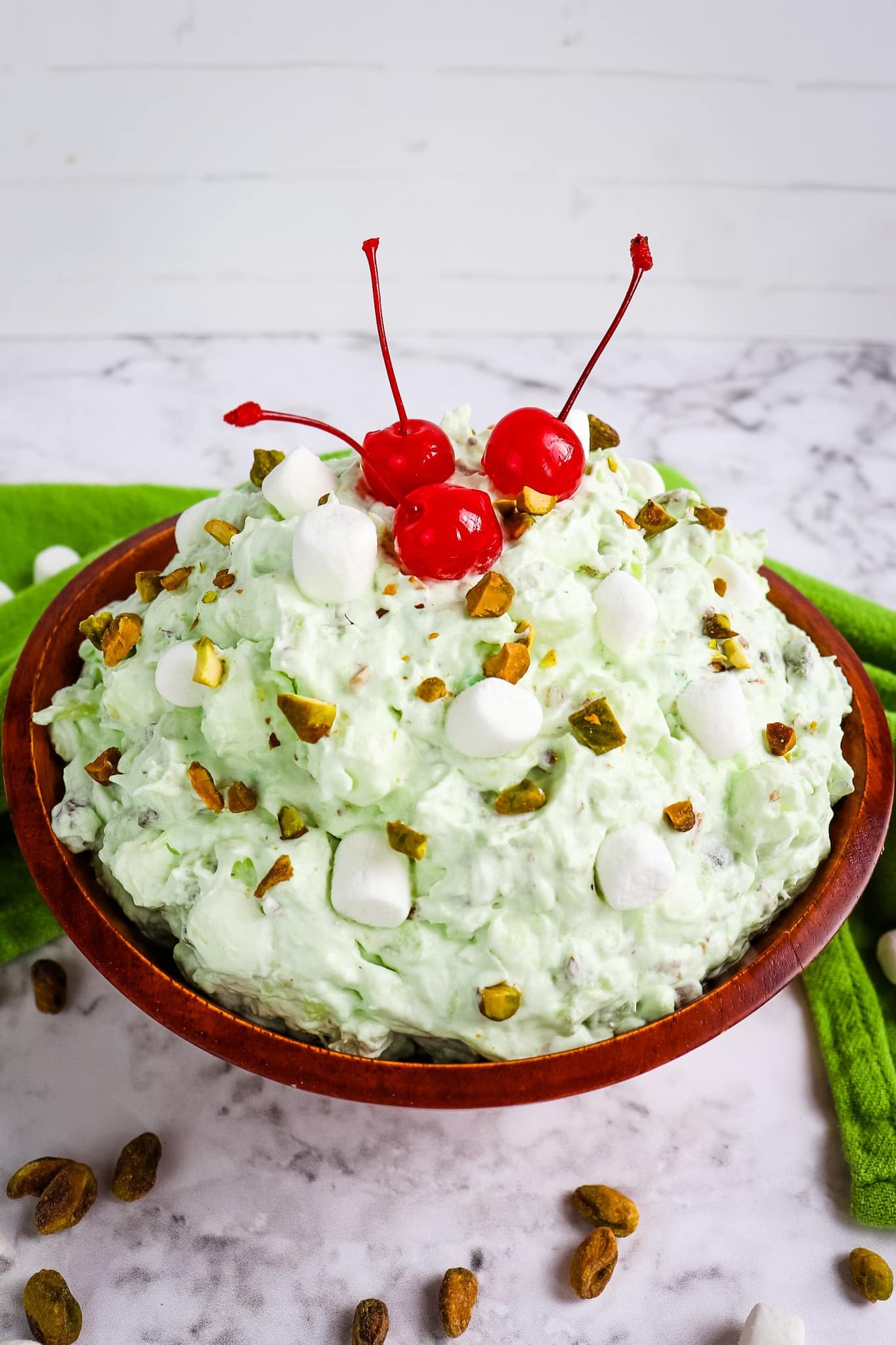 Pistachio fluff in a bowl topped with maraschino cherries and chopped pistachios.