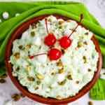 Pistachio fluff salad recipe in bowl topped with chopped pistachios and maraschino cherries.