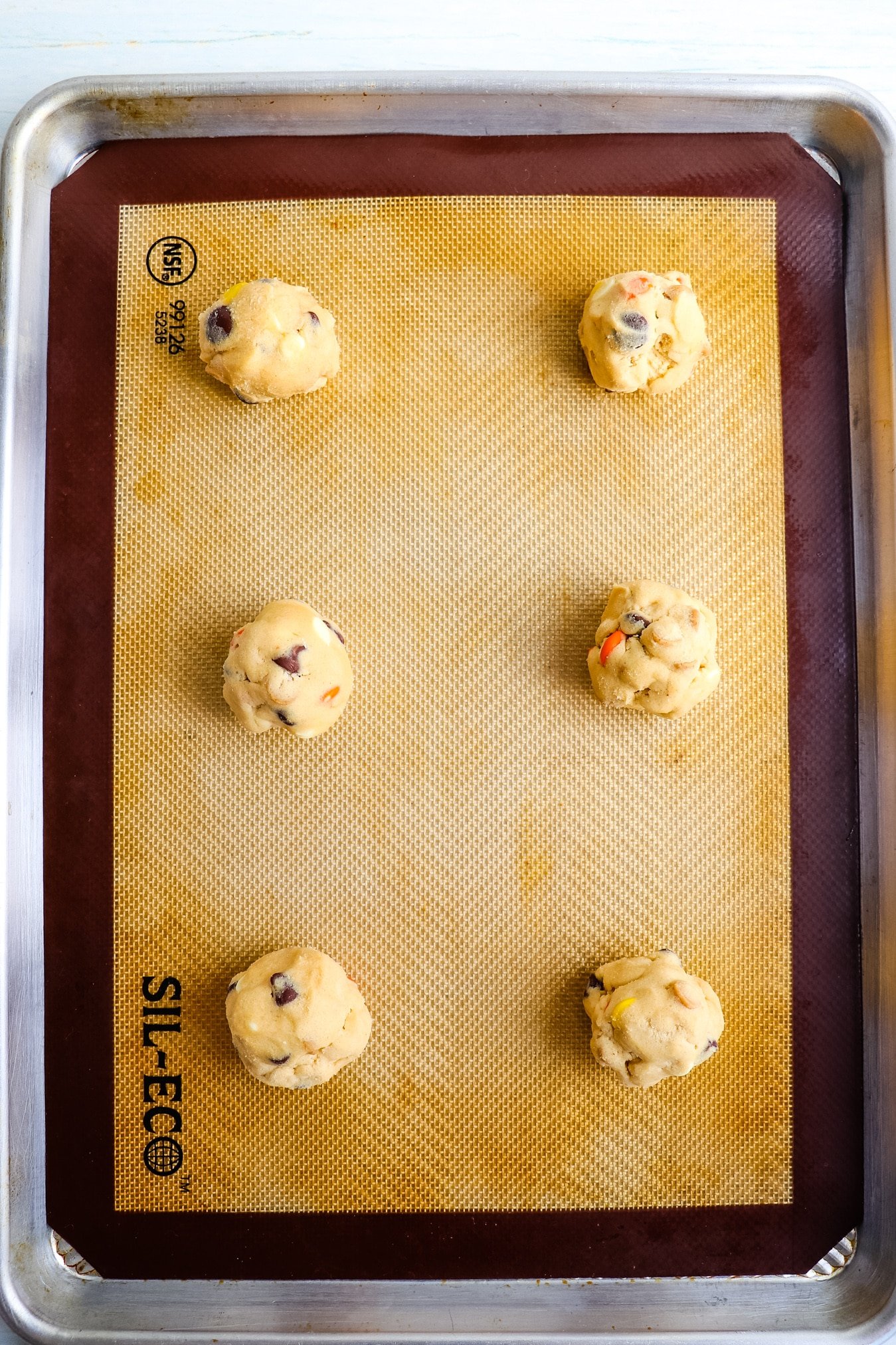 Six Reese's pieces cookies on a baking sheet, unbaked.