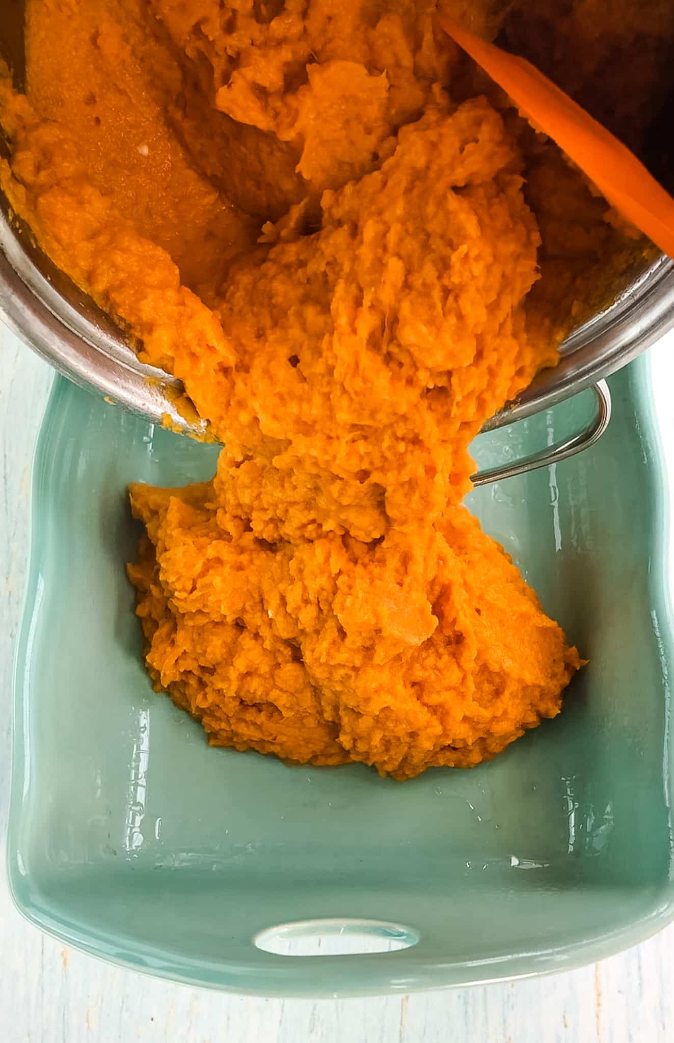 Mashed sweet potatoes being poured into a casserole dish.