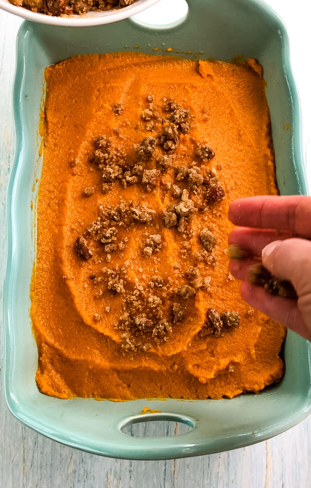 Pecan crumble topping being added to sweet potatoes.