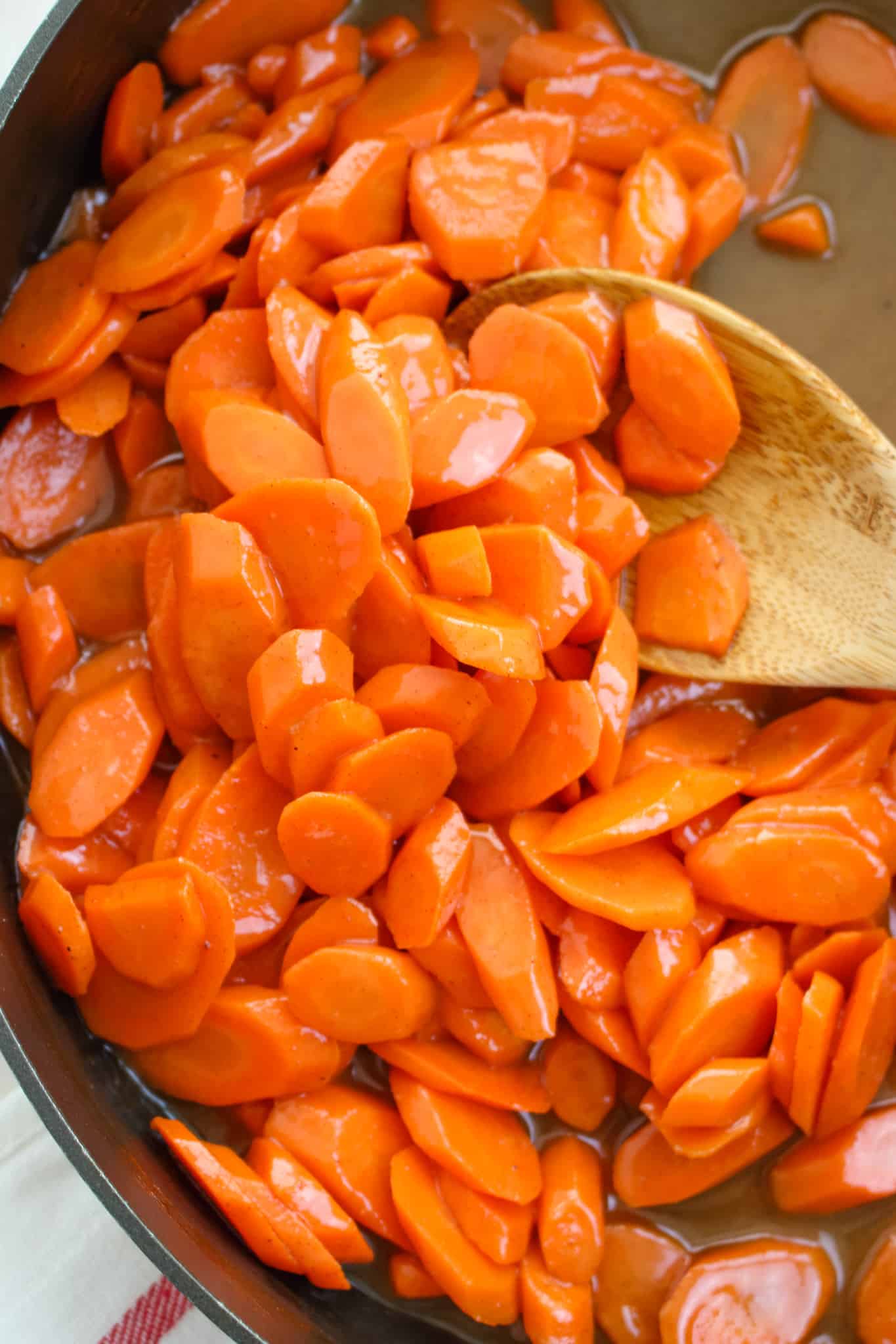 Sauteed carrots recipe in skillet with wooden spoon.