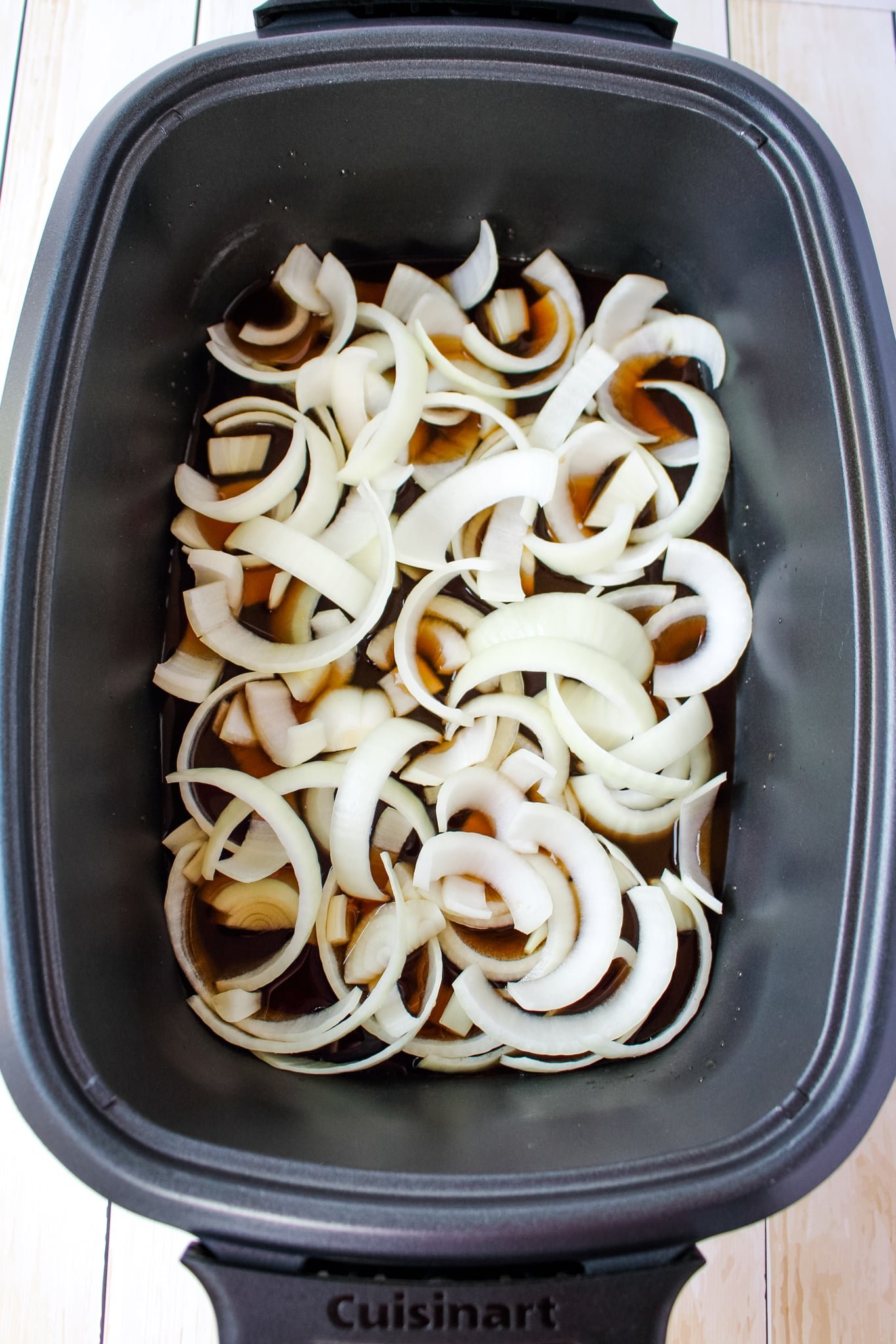 Slow cooker with onions and beef broth for slow cooker pulled beef recipe.