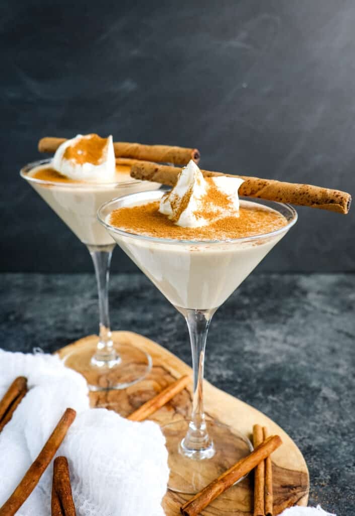 Two tiramisu martini drinks topped with cinnamon, whipped cream and a wafer cookie.