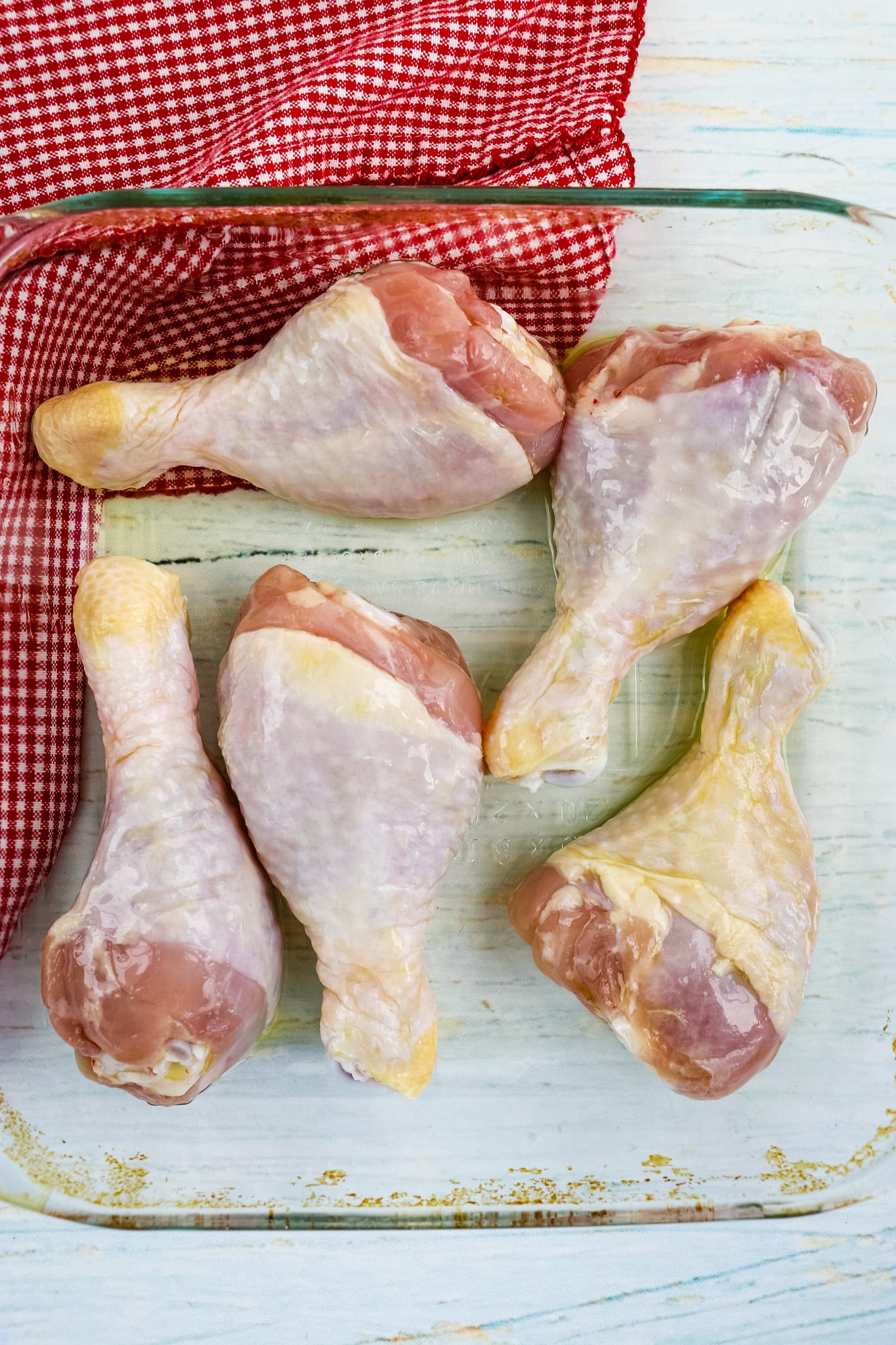 Chicken drumsticks in baking dish with olive oil.