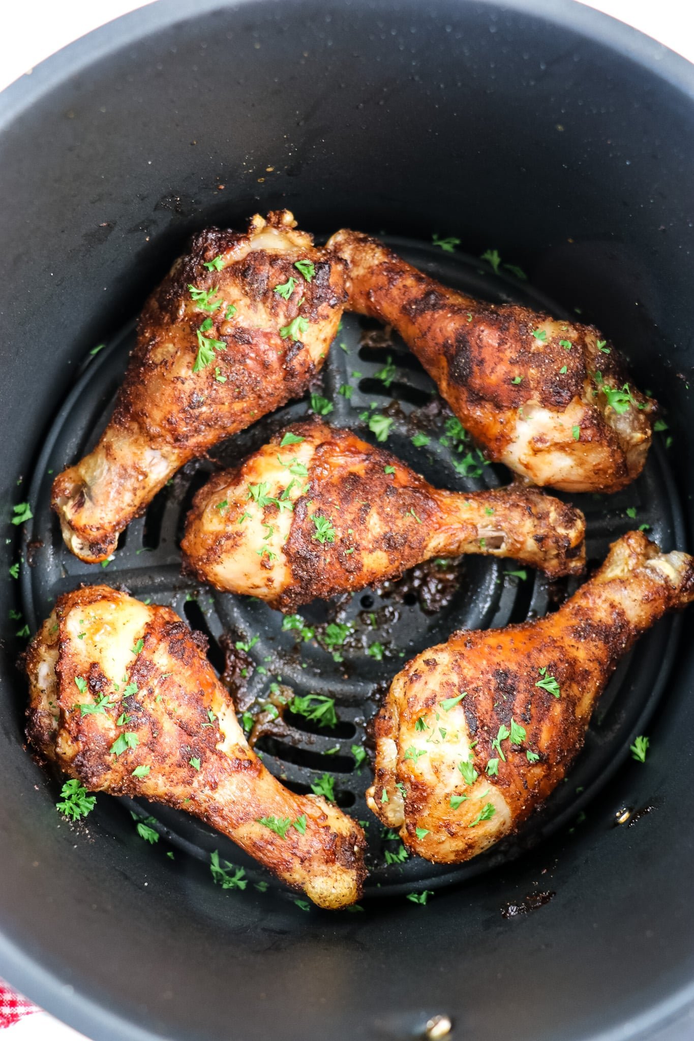 Drumsticks in air fryer after cooking, topped with fresh parsley.