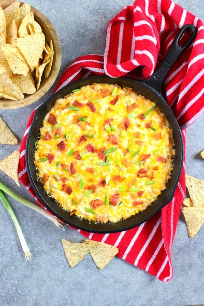 Cream cheese corn dip baked in a cast iron skillet and topped with bacon and green onions.
