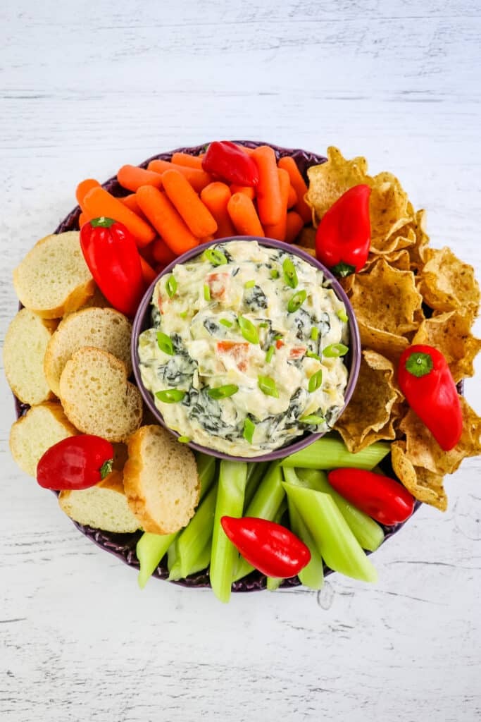 Carrots, celery, bread and tortilla chips being served with crock pot spinach artichoke dip.