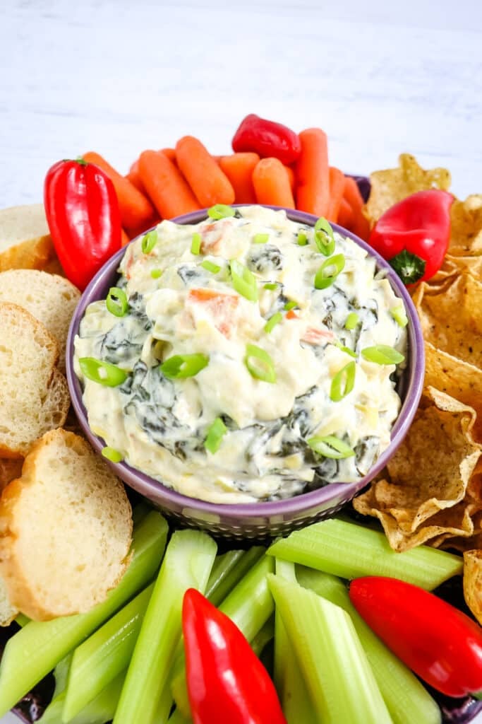 Hot spinach artichoke dip topped with sliced green onions and served with chips, bread and veggies.