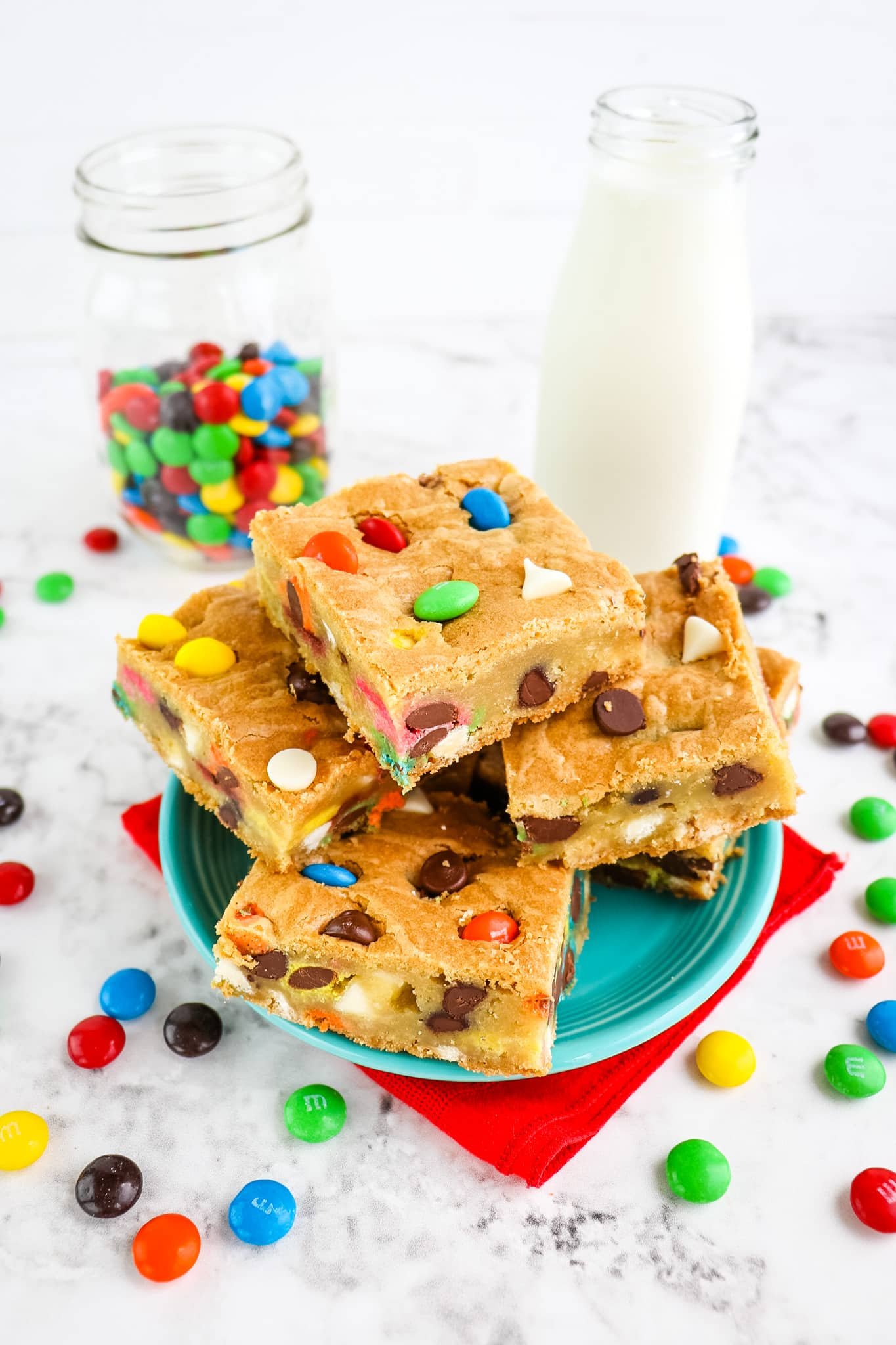 M&M cookie bars on a plate with milk and jar of M&M's in the background.