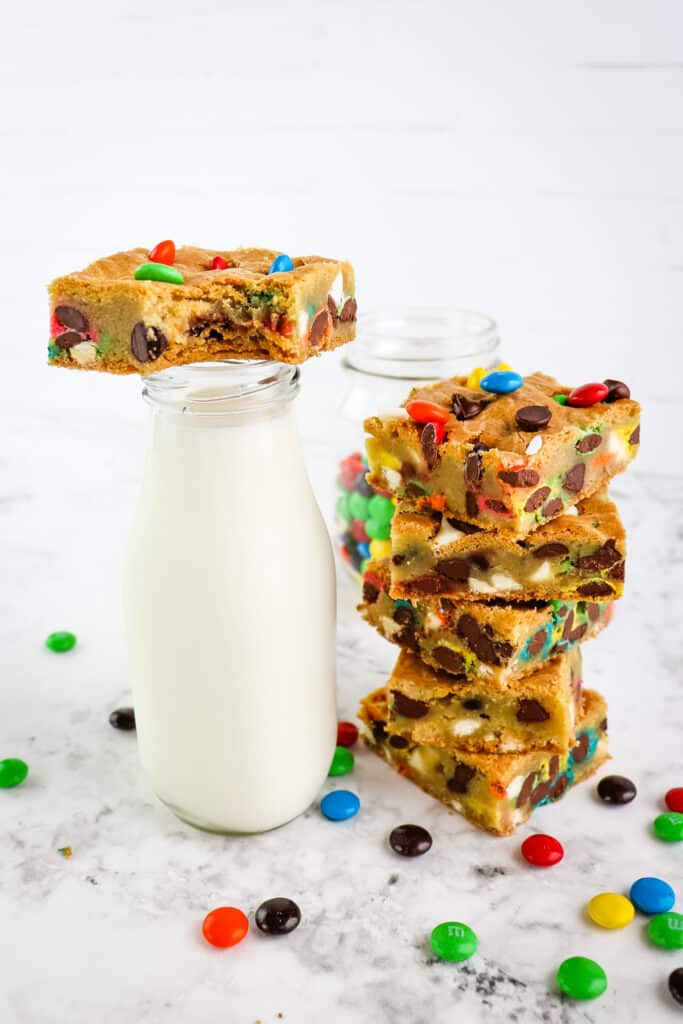 Stack of M&M bars along side a bottle of milk topped with a bar with a bite taken out.