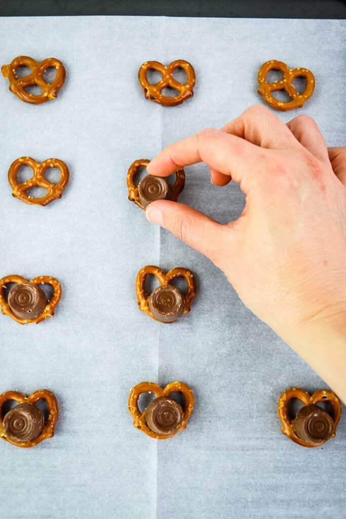 Placing a rolo on top of pretzels on a baking sheet.