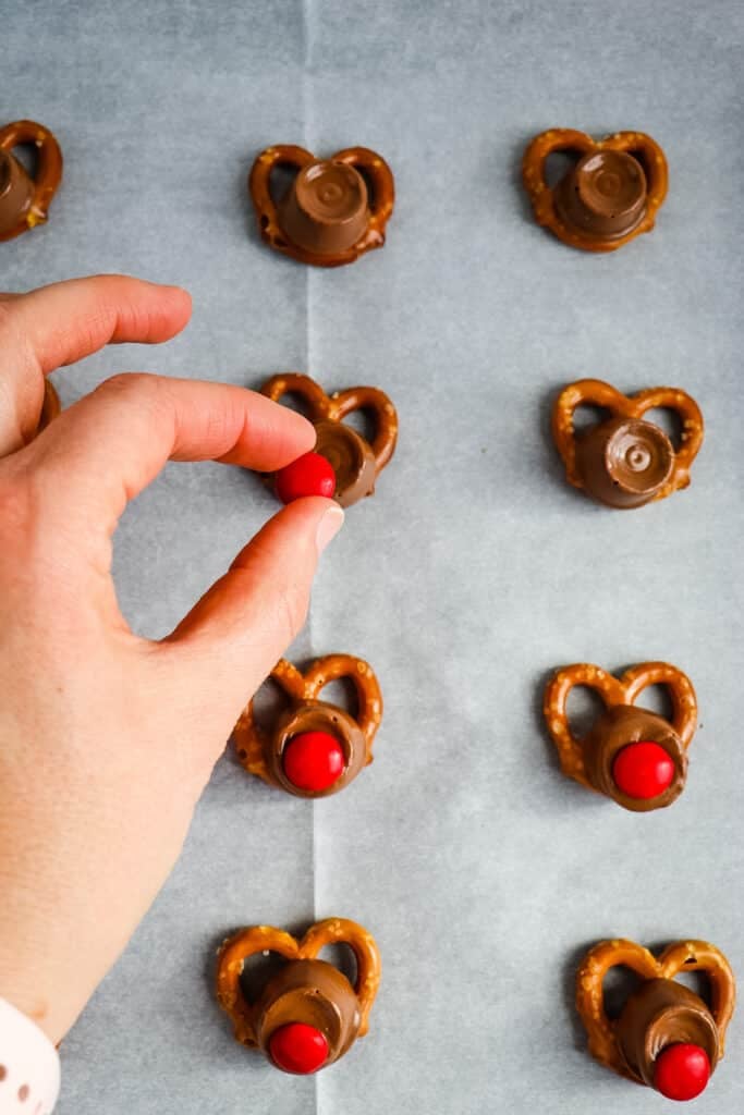 Placing a red M&M on top of rolo to make a rolo reindeer pretzels.