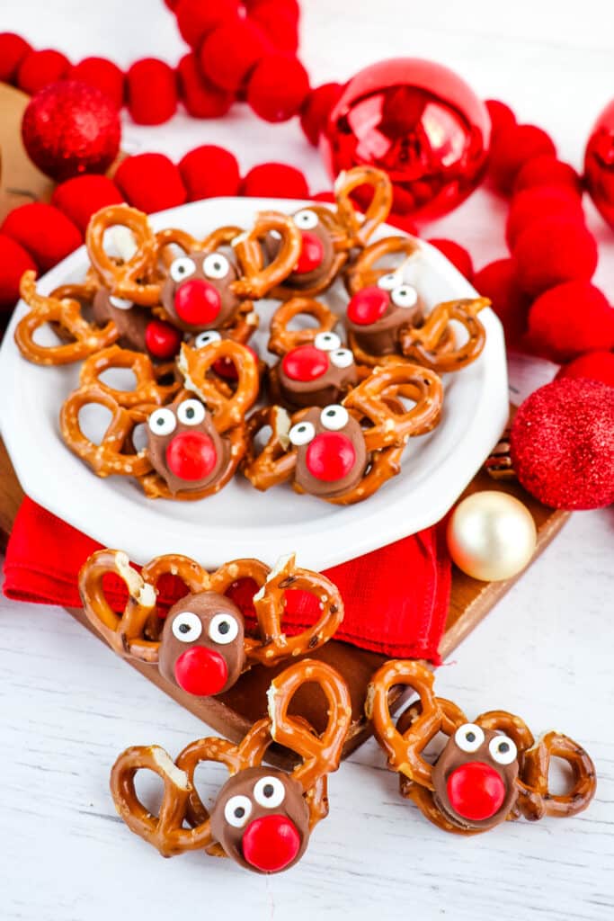 Reindeer pretzels on a white plate with Christmas decorations on the side.