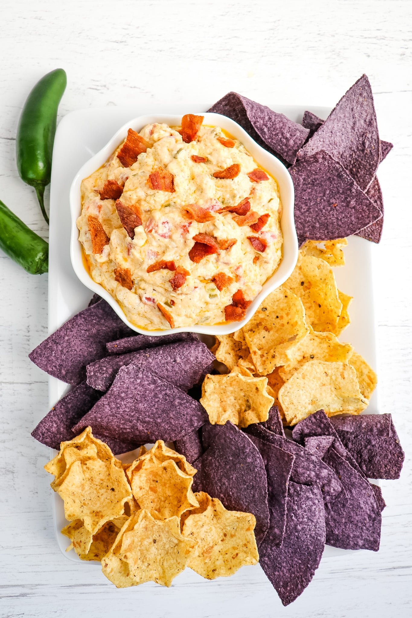 Hot jalapeno cream cheese dip in a bowl served with yellow and blue corn tortilla chips.