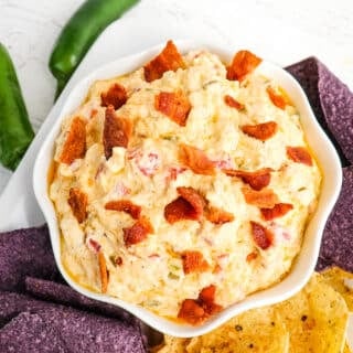 Crock pot jalapeno popper dip in a bowl topped with bacon and served with tortilla chips.