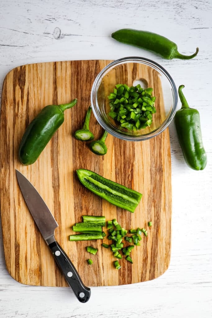 Fresh jalapeno peppers being chopped on a cutting board with knife on the side.