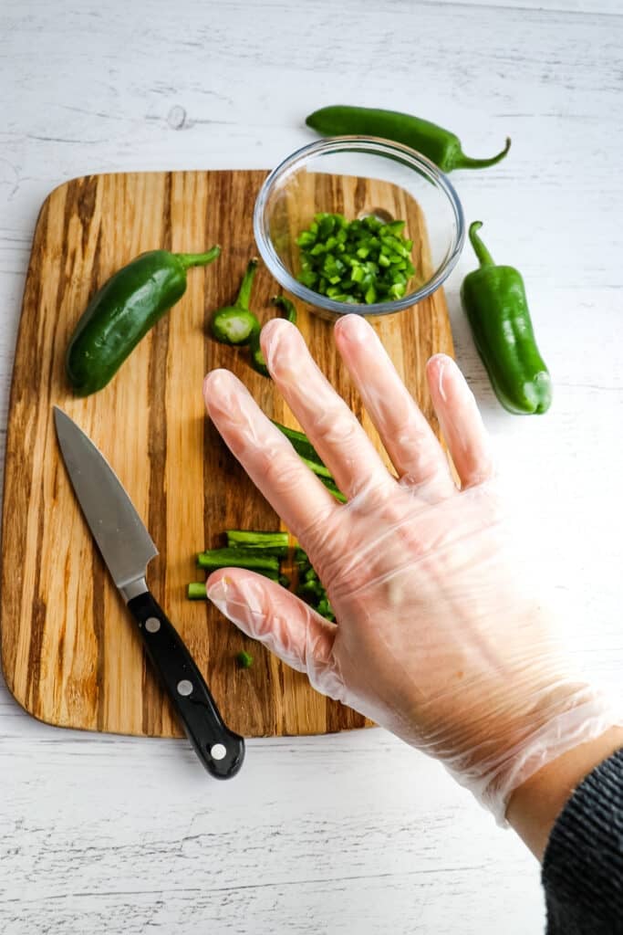 Hand with latex gloves being worn to chop jalapeno peppers.