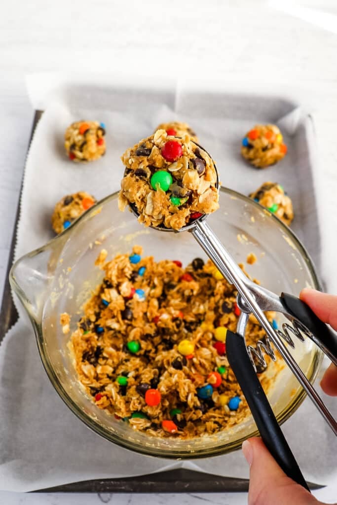 A cookie scoop being used to make oatmeal balls with M&M's.