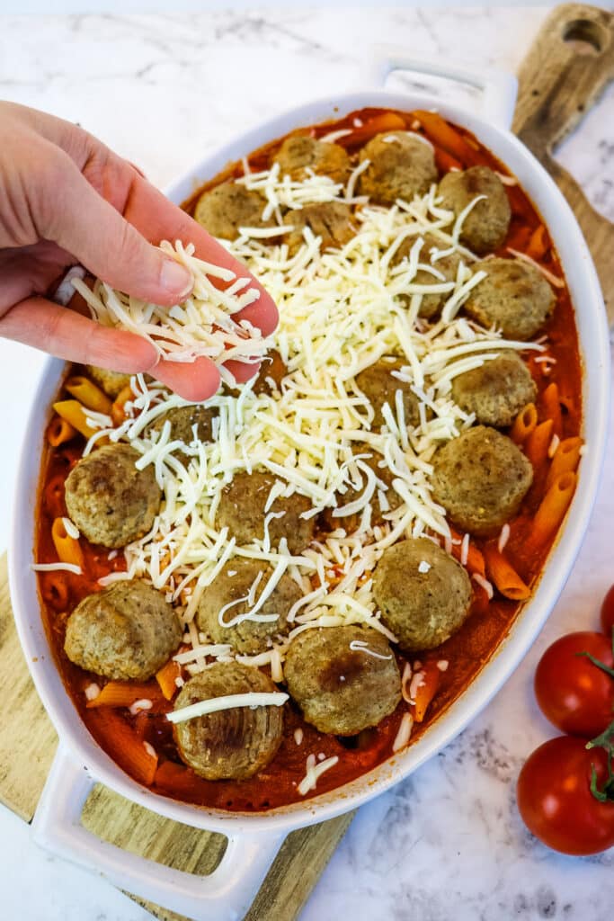 Shredded mozzarella cheese being added to the top of meatball casserole recipe.