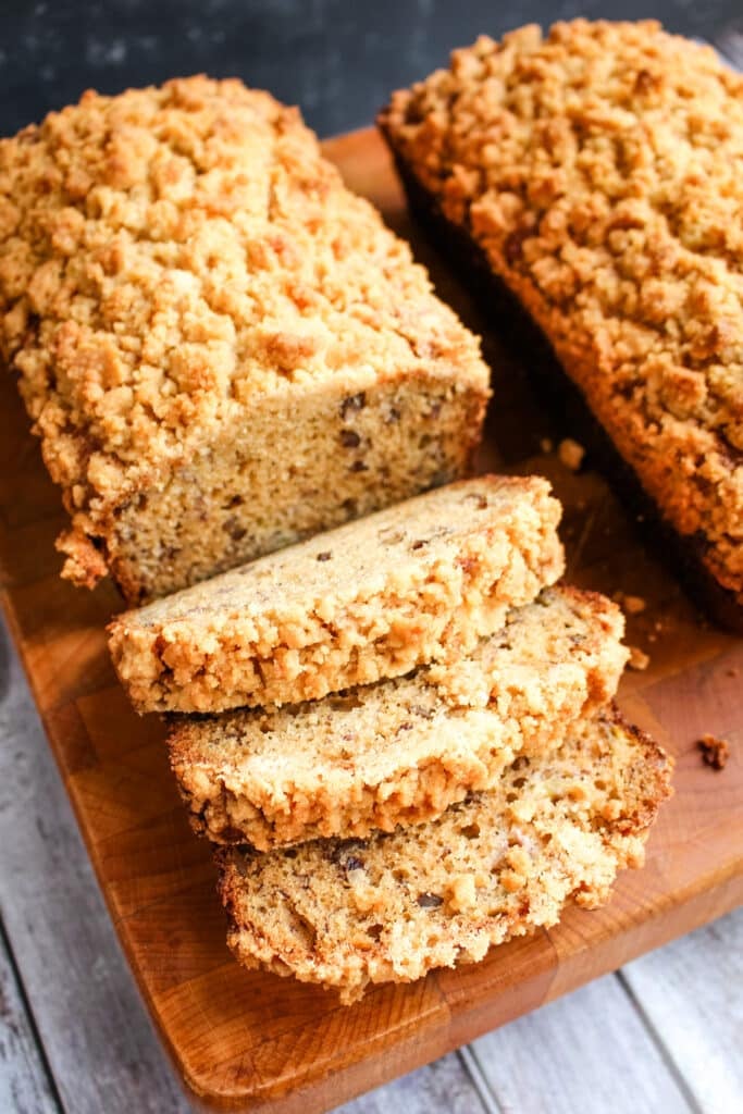 Two loaves of banana bread on a cutting board with one loaf sliced three times.