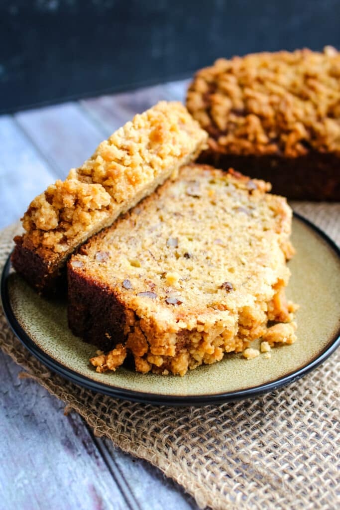 Two slices of award winning banana bread on a plate with full loaf in the background.