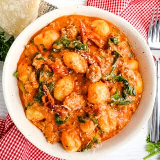 Creamy gnocchi and sausage recipe in a bowl topped with grated Parmesan cheese.