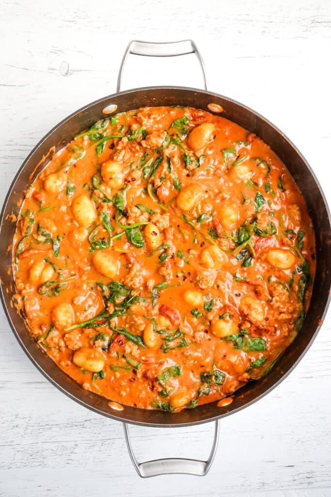 Finished sausage gnocchi in creamy red sauce with spinach.