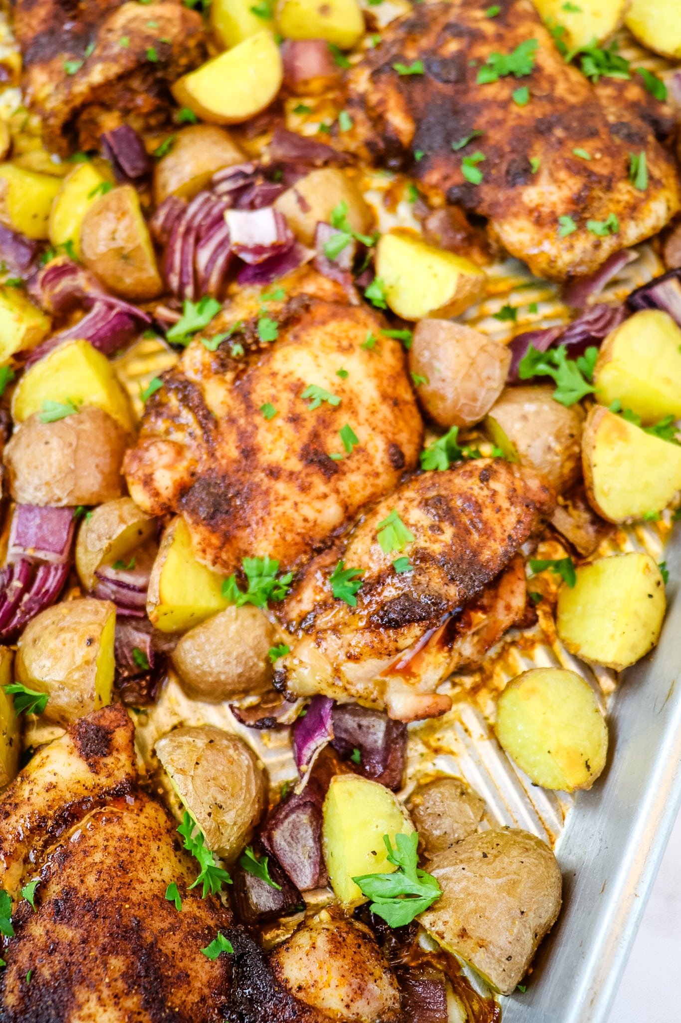 Roasted chicken thighs and potatoes on sheet pan topped with chopped parsley.