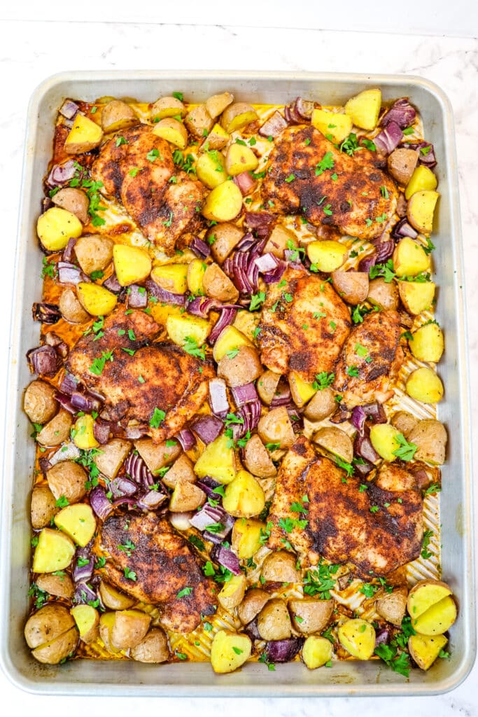 Sheet pan chicken thighs with potatoes and red onions, topped with chopped parsley.