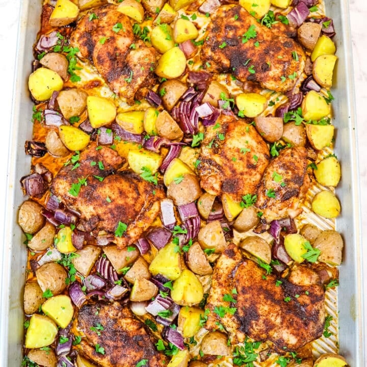Sheet pan chicken thighs with potatoes and red onions, topped with chopped parsley.